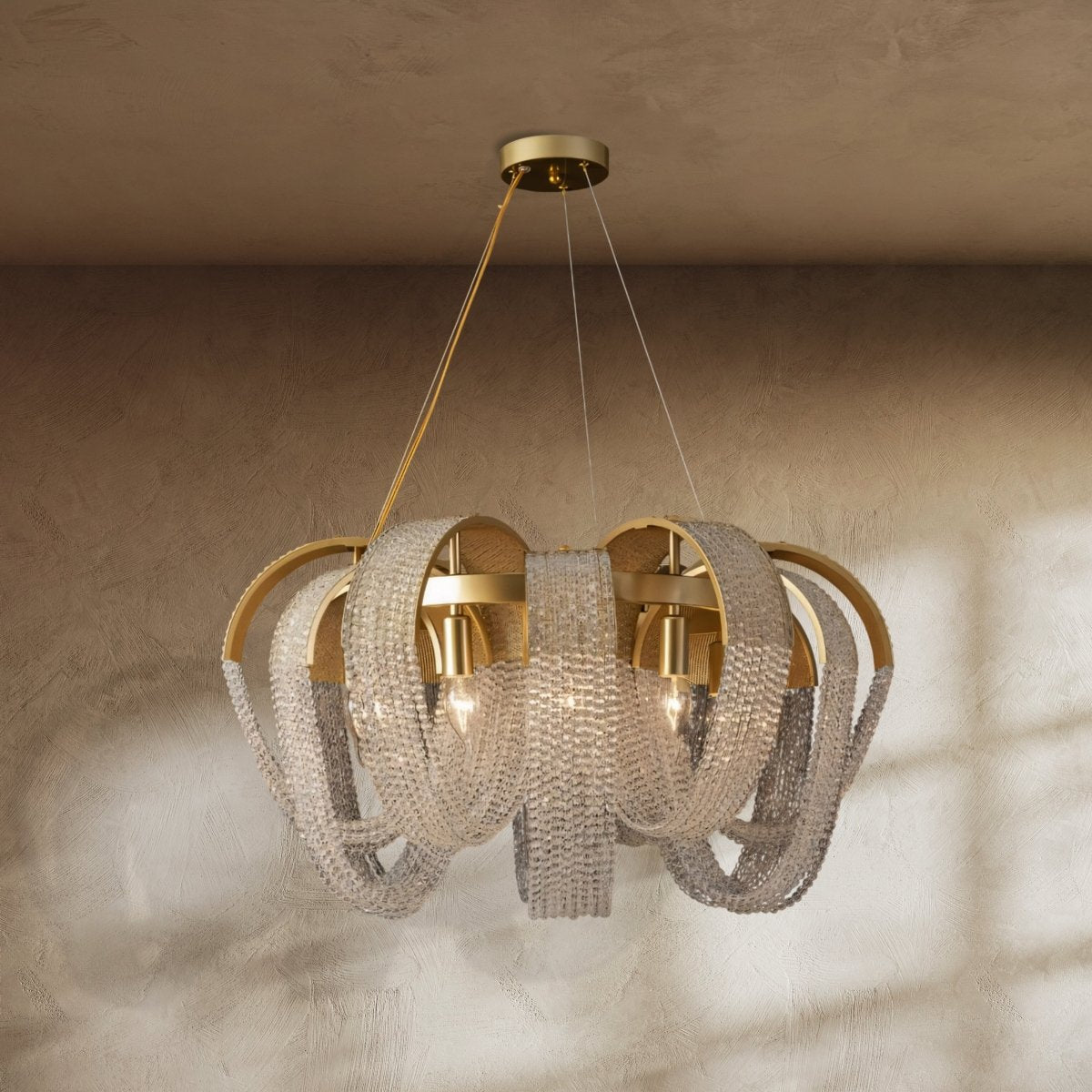 Clérachic gold chandelier hung with looping crystal bead chains over brass arches, lit with candle bulbs against a plaster wall.