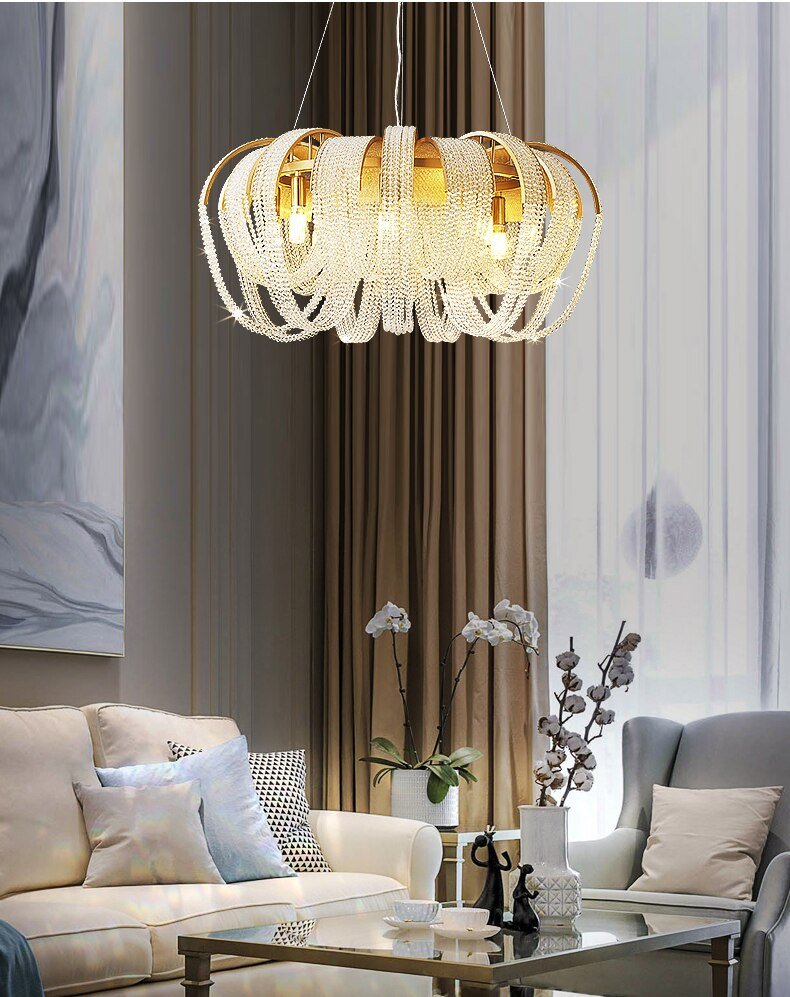 Clérachic gold chandelier with swags of crystal beads, lit above a glass coffee table in a living room with a cream sofa.
