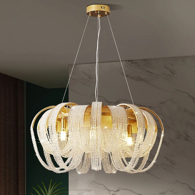 Clérachic gold chandelier with looping crystal bead chains, lit in a room with a marble feature wall and deep green panel.