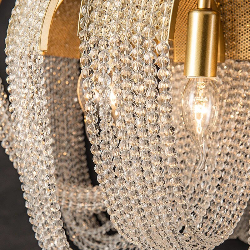 Clérachic close view of faceted crystal bead chains looped between brass arches, with a candle bulb in a brass socket.