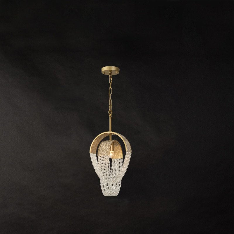 Clérachic single-head gold pendant with a brass arch and crystal bead chains on a chain suspension, against a dark backdrop.