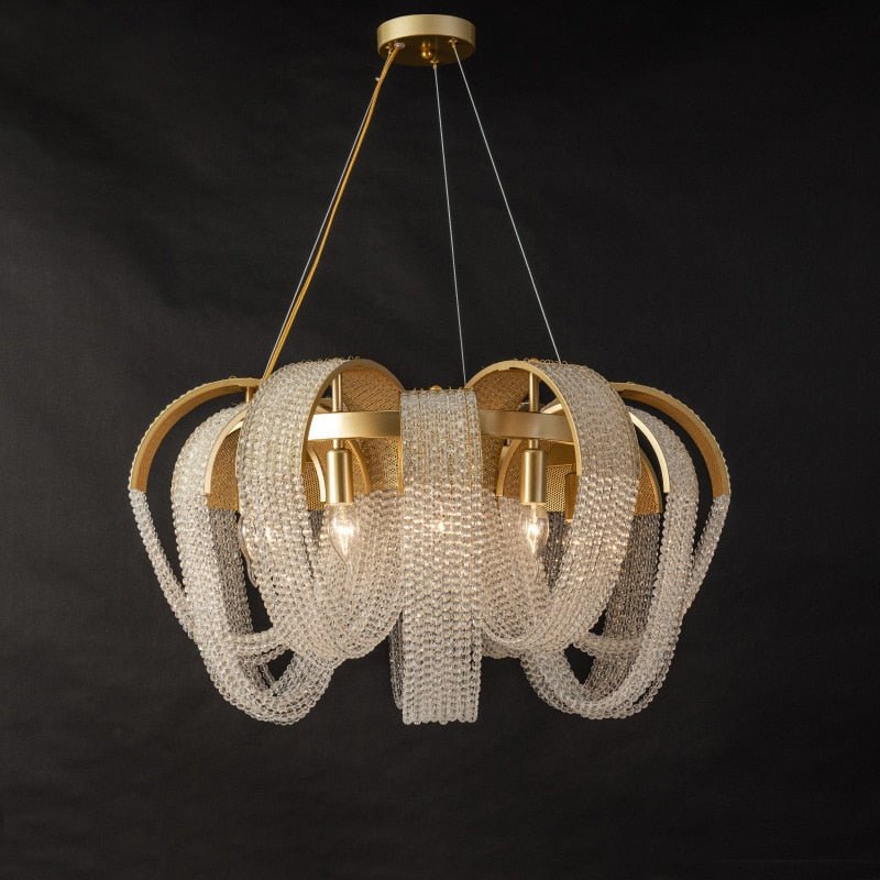 Clérachic multi-head gold chandelier with crystal bead loops and visible candle bulbs on brass arches, on a dark backdrop.