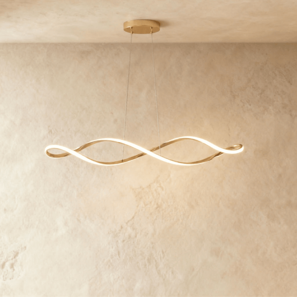 Clérachic chandelier in gold, its twisting ribbon of light glowing against a plaster wall.