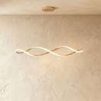 Clérachic chandelier in gold, its twisting ribbon of light glowing against a plaster wall.
