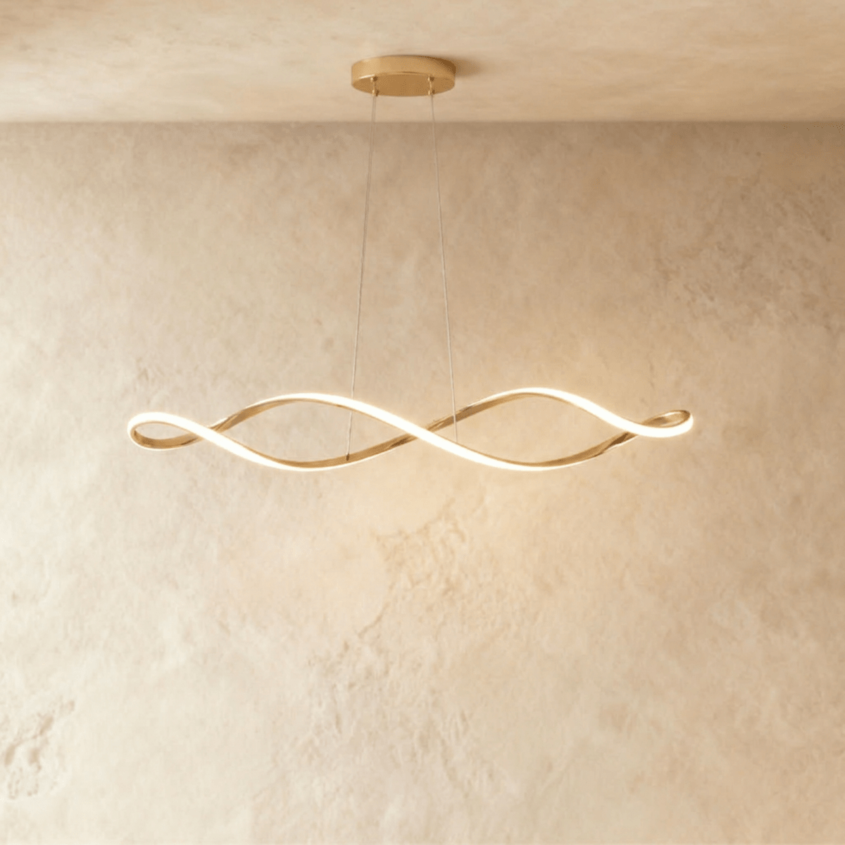 Clérachic chandelier in gold, its twisting ribbon of light glowing against a plaster wall.