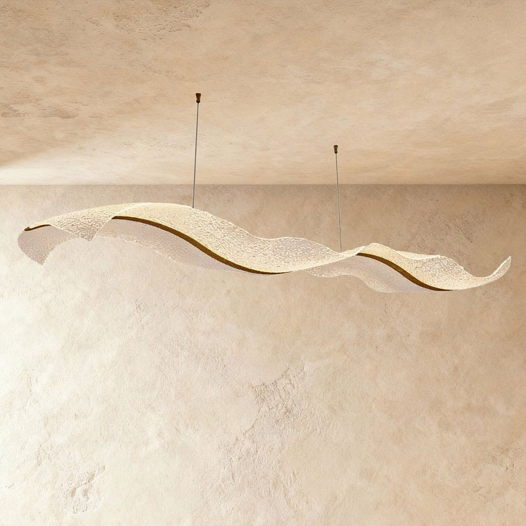 Clérachic's gold ribbon chandelier curves in a double wave shape, its textured acrylic catching soft plaster light.