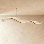 Clérachic's gold ribbon chandelier curves in a double wave shape, its textured acrylic catching soft plaster light.