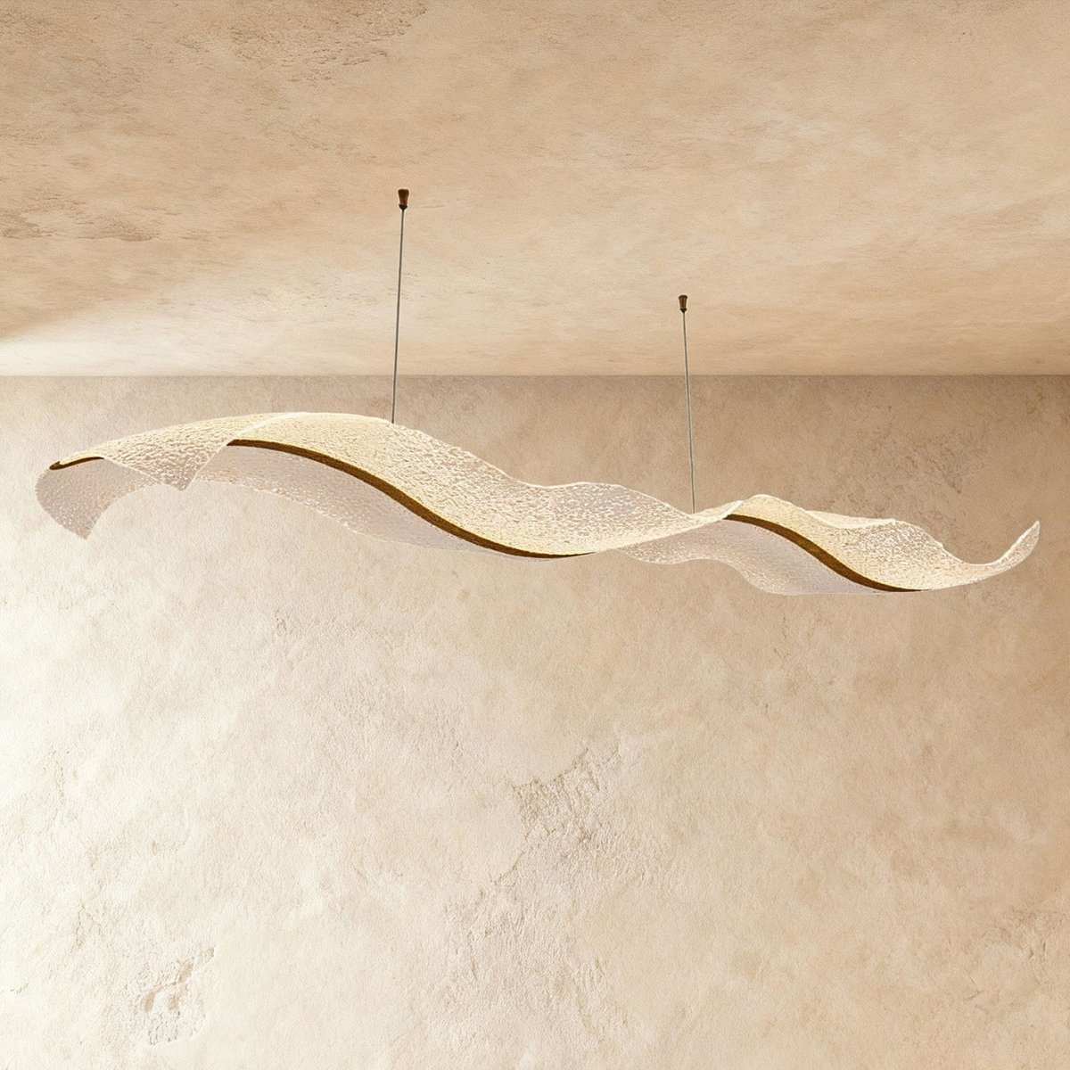 Clérachic's gold ribbon chandelier curves in a double wave shape, its textured acrylic catching soft plaster light.