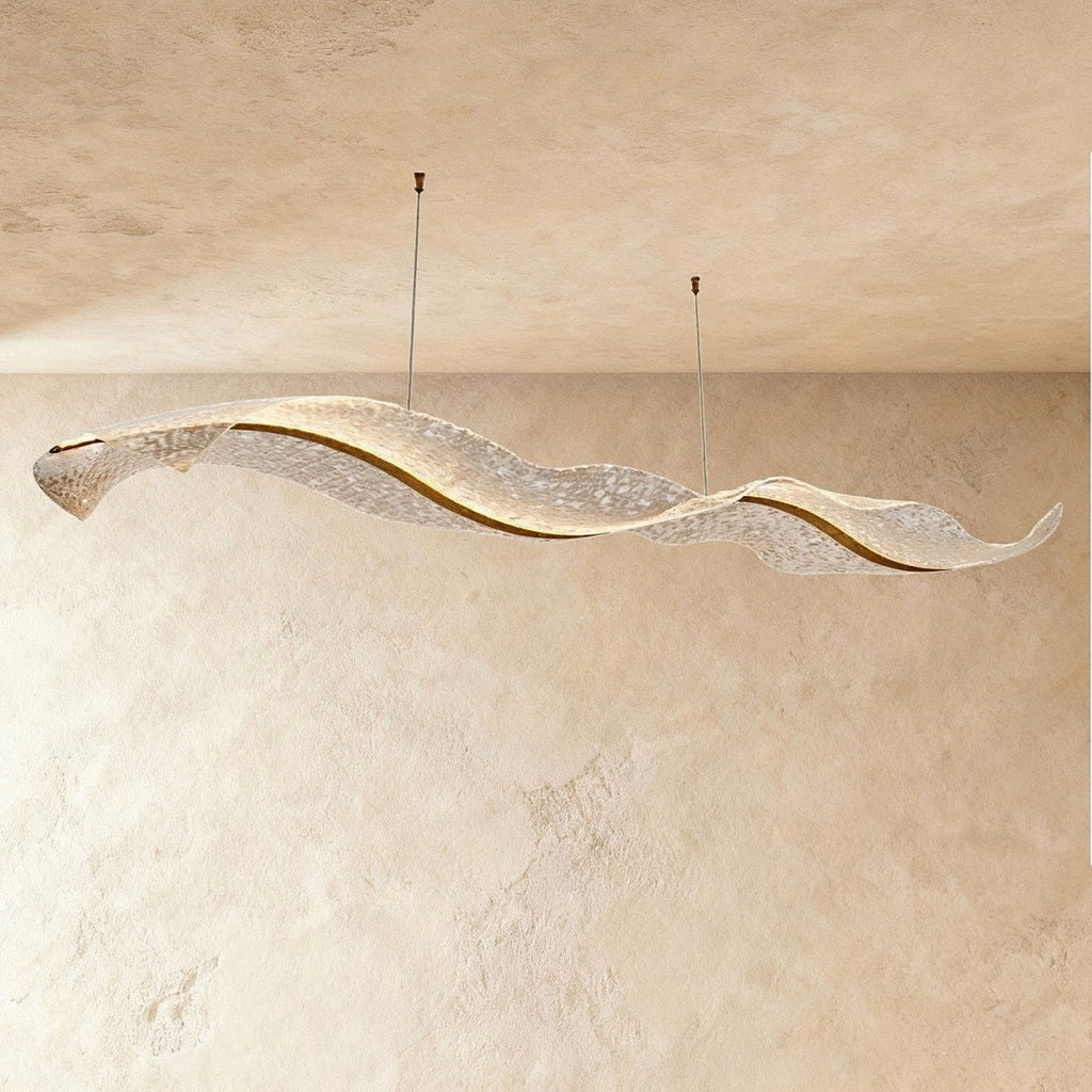 A wide view of the Clérachic wave chandelier shows its rippling acrylic form against a plaster wall.