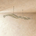 Clérachic's ribbon chandelier glows along a glassy frosted surface in its long double-wave shape.