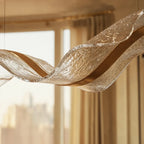 Close-up of the lit Clérachic chandelier shows its glittering textured surface against a city-view window.