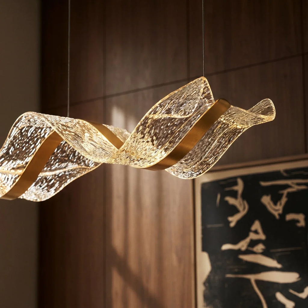 Close-up of the lit Clérachic chandelier's gold ribbon form against dark walnut wall panelling.