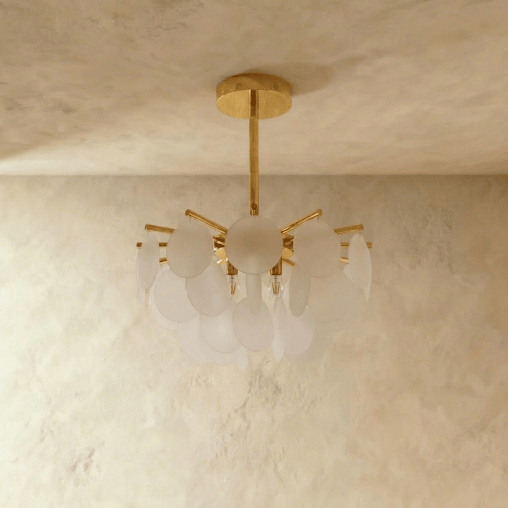 Clérachic Isla chandelier, frosted glass discs clustered around a brass frame, hung from a textured plaster ceiling.