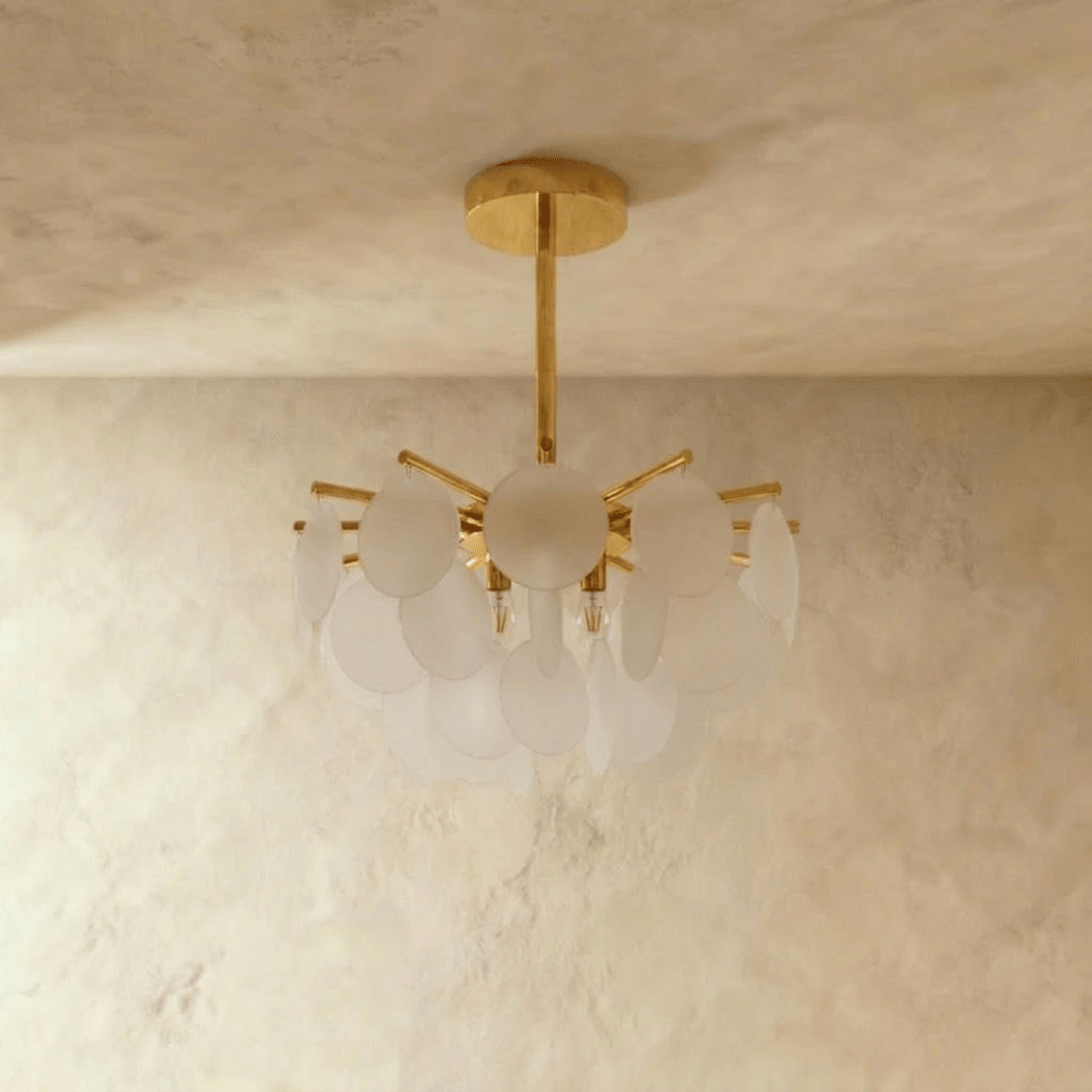 Clérachic Isla chandelier, frosted glass discs clustered around a brass frame, hung from a textured plaster ceiling.