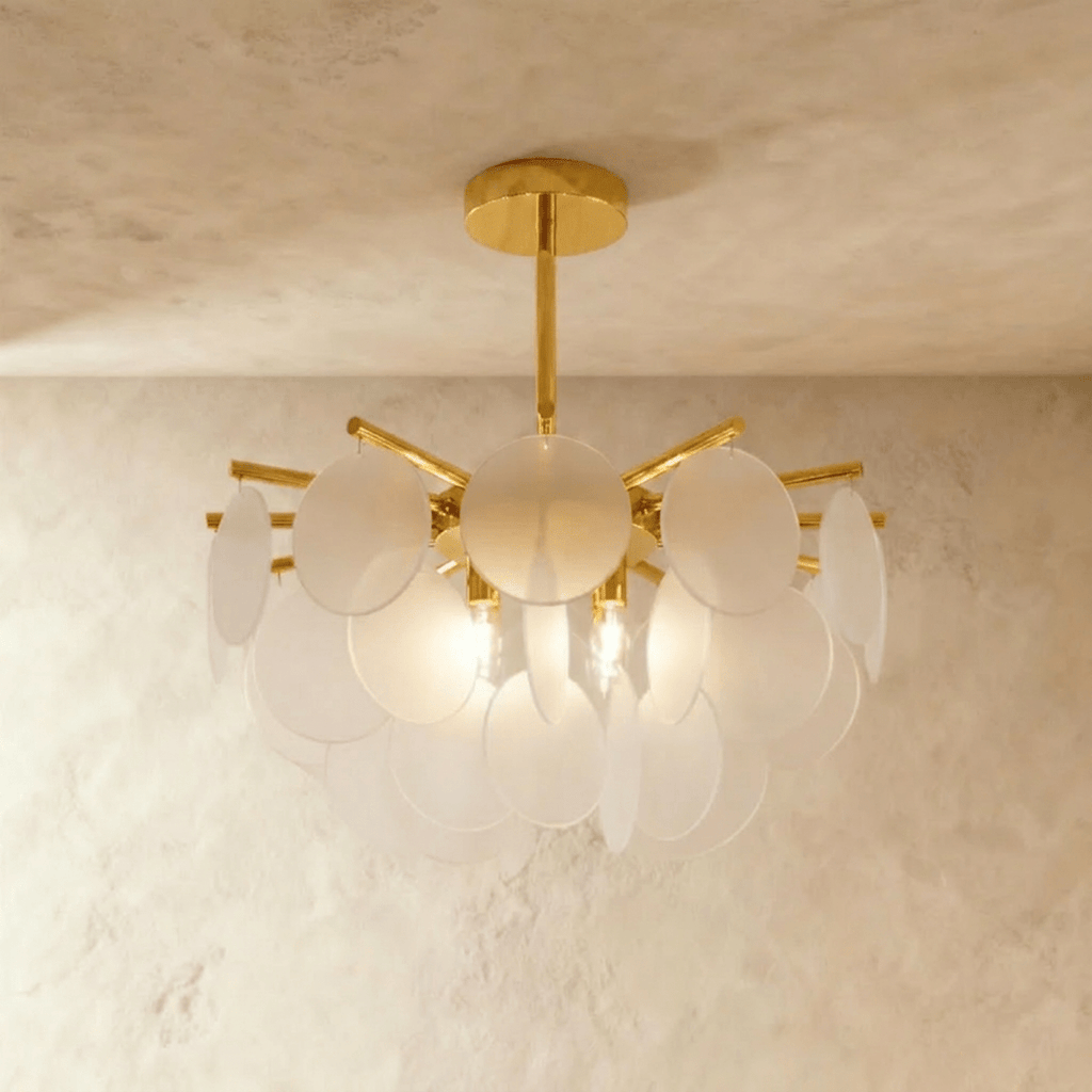 Clérachic Isla chandelier lit warm, frosted translucent glass discs glowing around a brass fixture on a plaster wall.