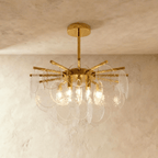 Clérachic Isla chandelier lit warm in clear transparent glass, hammered-texture discs fanned from a brass frame.
