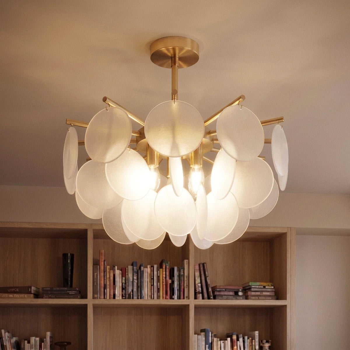 Clérachic Isla chandelier in translucent glass lit warm above a built-in bookcase, brass stem on a plain ceiling.