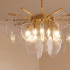 Clérachic Isla chandelier detail, hammered clear glass discs catching light around the brass frame and bulbs.