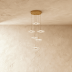 Clérachic staircase chandelier in gold, six glowing flower-shaped discs spiralling down at staggered heights.