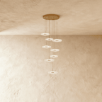 Clérachic staircase chandelier in gold, its cascading flower-shaped discs staggered down a plaster stairwell wall.