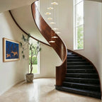 Clérachic staircase chandelier in gold cascading beside a curved wood staircase, its discs glowing above a marble floor.