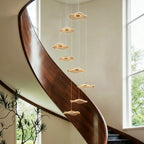 Clérachic staircase chandelier in gold, glowing discs cascading close beside a polished curved wooden staircase rail.