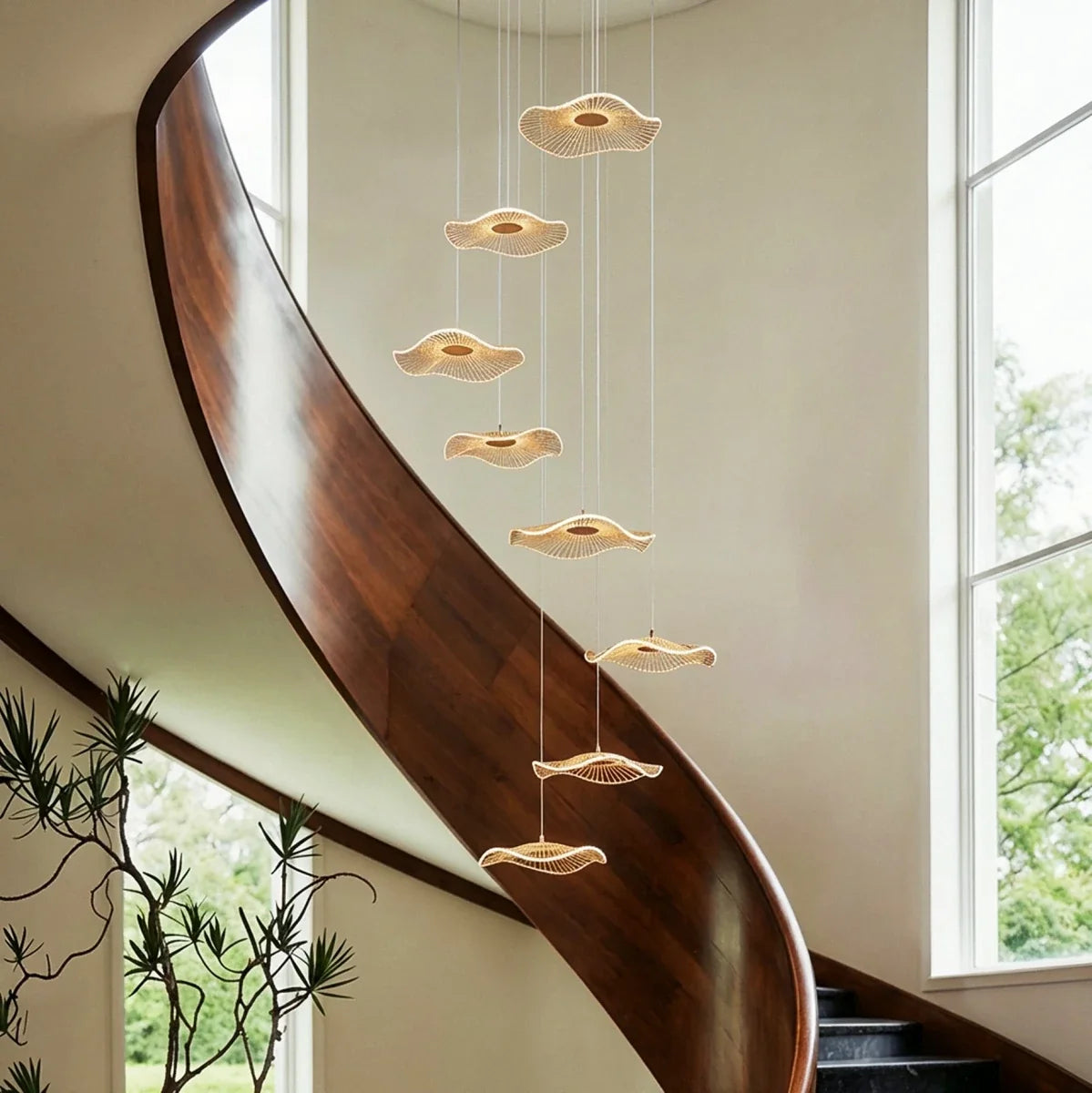 Clérachic staircase chandelier in gold, glowing discs cascading close beside a polished curved wooden staircase rail.