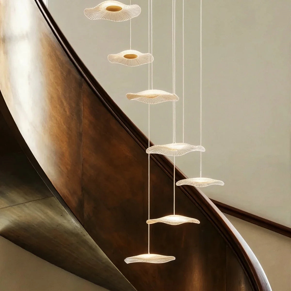 Close-up of the Clérachic staircase chandelier's discs cascading beside a dark polished curved staircase rail.