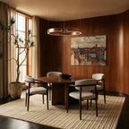 A rose gold Clérachic ring chandelier hangs low over a round walnut dining table in a wood-paneled room.