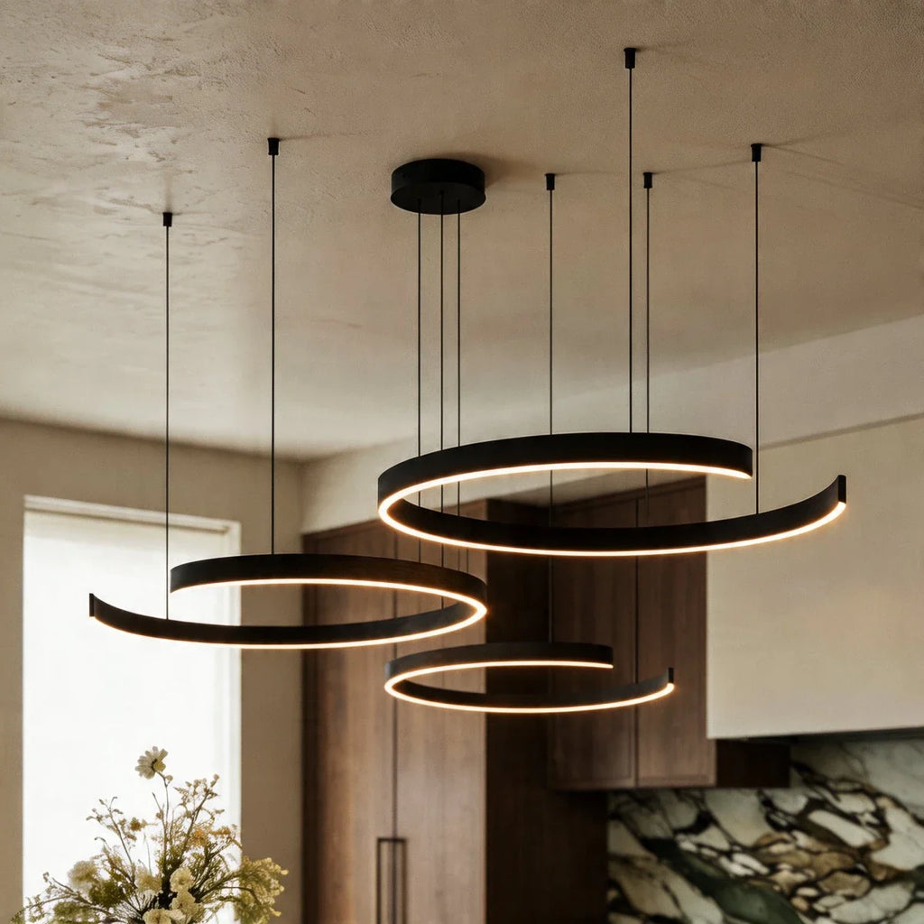 This matte black Clérachic three-ring chandelier casts warm light over a marble island and green backsplash.