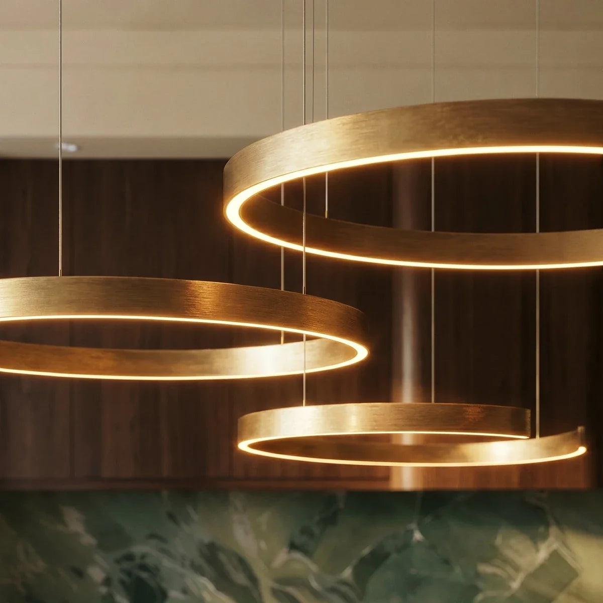 A close view shows the Clérachic chandelier's brushed gold rings glowing warmly above a green marble counter.