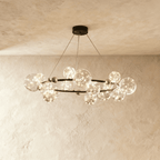 Clérachic chandelier in black, clear glass globes with warm fairy-light filaments ringing a round brass-dotted frame.