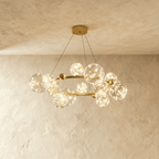 Clérachic chandelier in gold, its ring of glass bubble globes glowing warm white beneath a plaster ceiling.