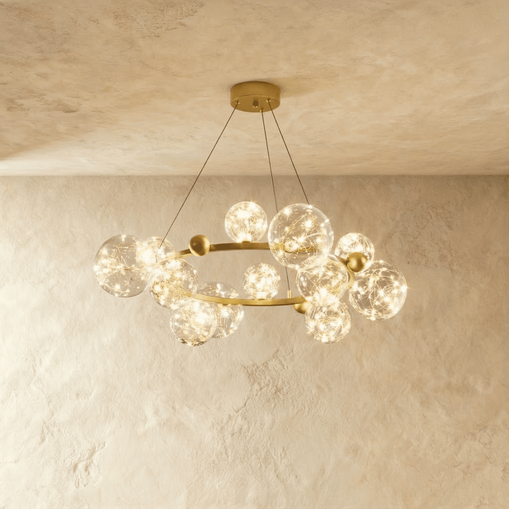 Clérachic chandelier in gold, its ring of glass bubble globes glowing warm white beneath a plaster ceiling.