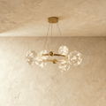 Clérachic chandelier in gold with fewer glass globes clustered around the round frame, glowing warm white.