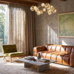 Clérachic chandelier in gold suspended over a leather sofa, its glowing glass globes ringing a brass frame.