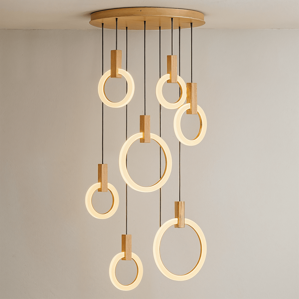Clérachic cluster of seven lit acrylic rings with oak blocks hung from a round wooden canopy on black cords.