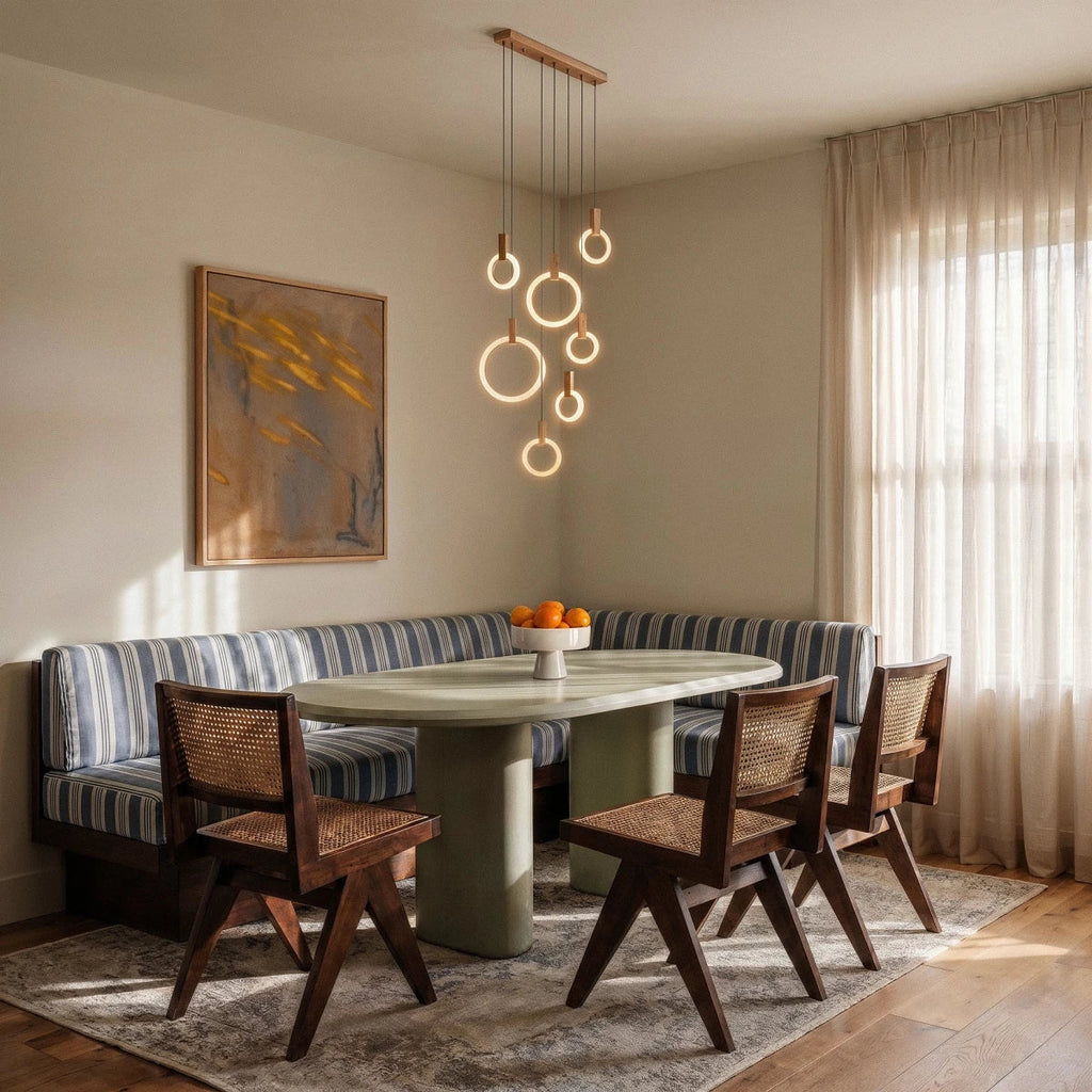 Clérachic cluster of lit acrylic rings hung from a long wooden canopy above an oval table and striped banquette seating.