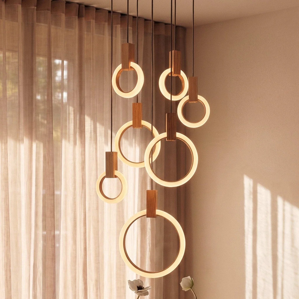 Clérachic seven lit acrylic rings with oak blocks at varied heights, seen close up beside sheer linen curtains.
