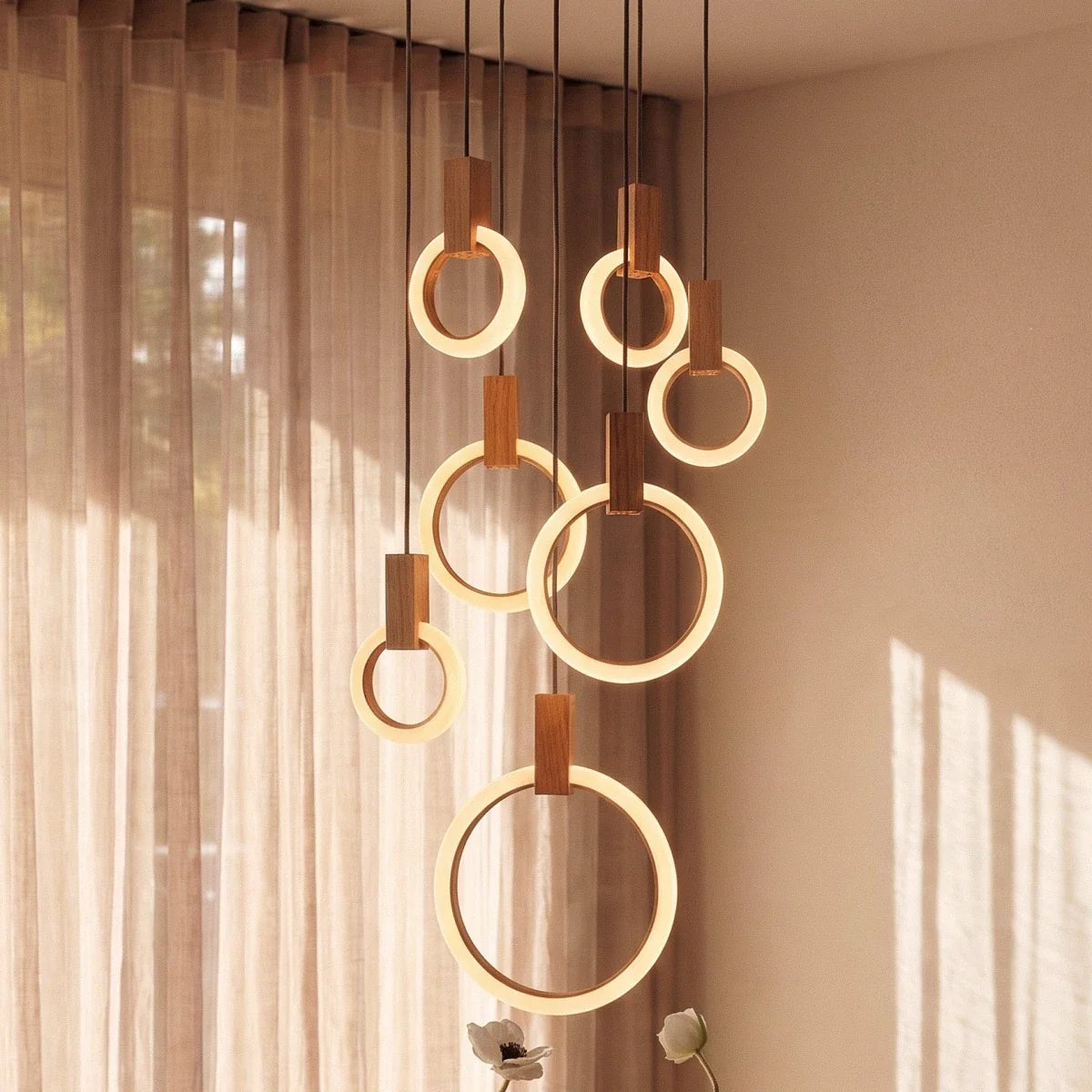 Clérachic seven lit acrylic rings with oak blocks at varied heights, seen close up beside sheer linen curtains.