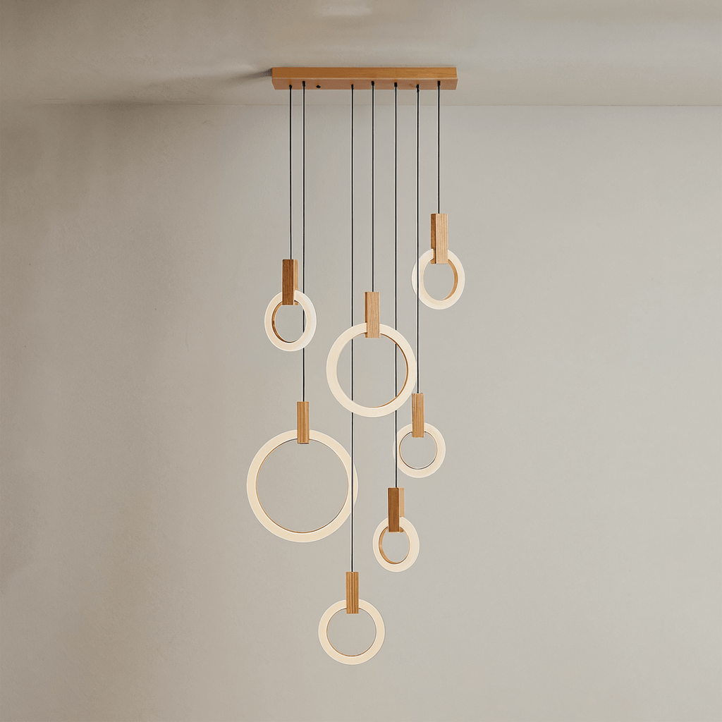 Clérachic seven lit acrylic rings with oak blocks hung from a long oak canopy on black cords against a grey wall.
