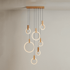 Clérachic seven lit acrylic rings with oak blocks hung from a long oak canopy on black cords against a grey wall.
