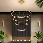 Clérachic gold four-ring LED chandelier in graduated sizes above a dark fluted fireplace wall, with palms and brass sconces.