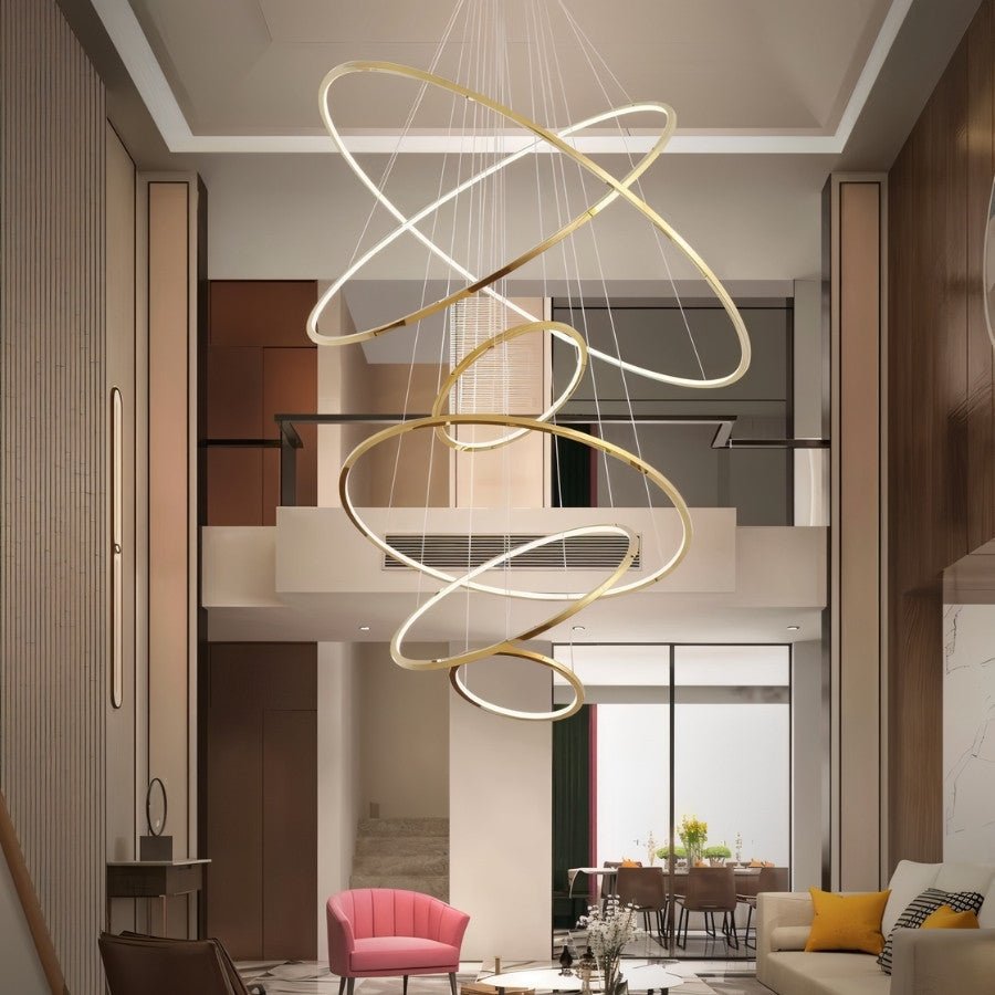 Clérachic gold multi-ring LED chandelier of crossed rings dropping through a double-height living room with a pink armchair.