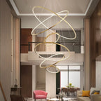 Clérachic gold multi-ring LED chandelier of crossed rings dropping through a double-height living room with a pink armchair.