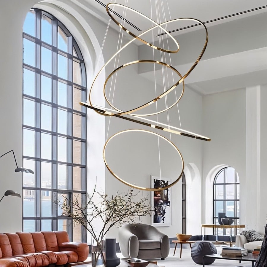 Clérachic gold LED ring chandelier of tilted rings hanging in a tall arched-window living room above a leather sofa.