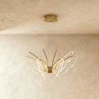 Clérachic gold-finished butterfly chandelier with clear acrylic wings fanning from a central hub on a limewash backdrop.