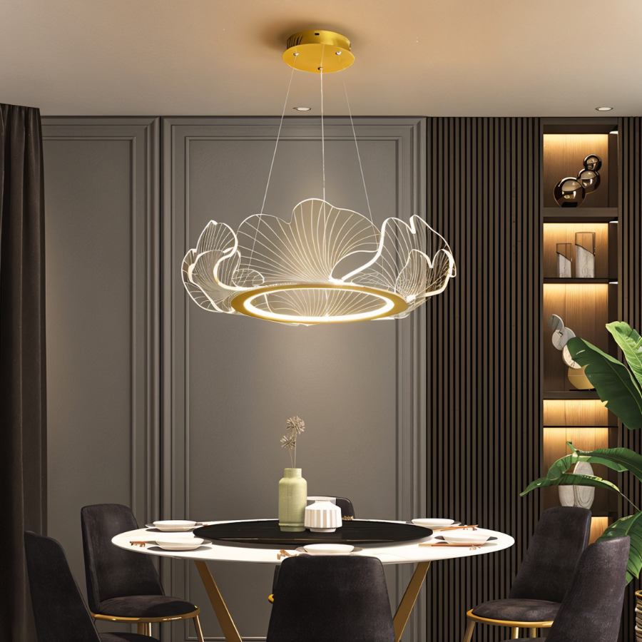 Clérachic gold and clear acrylic leaf chandelier glowing over a round marble dining table in a deep grey panelled room.