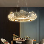Clérachic lit leaf chandelier with veined acrylic petals and a gold ring, above a dining table in a green-grey room.
