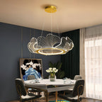 Clérachic gold-ringed leaf chandelier with clear acrylic petals hanging over a round dining table in a dark green room.